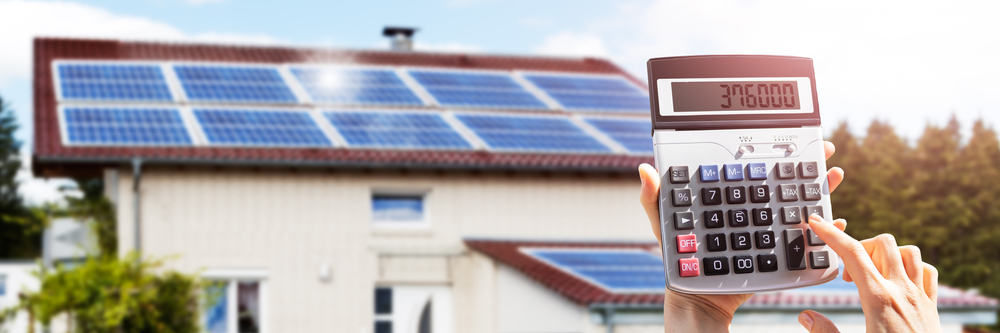 Calculator held up in front of a house with solar panels on the roof.